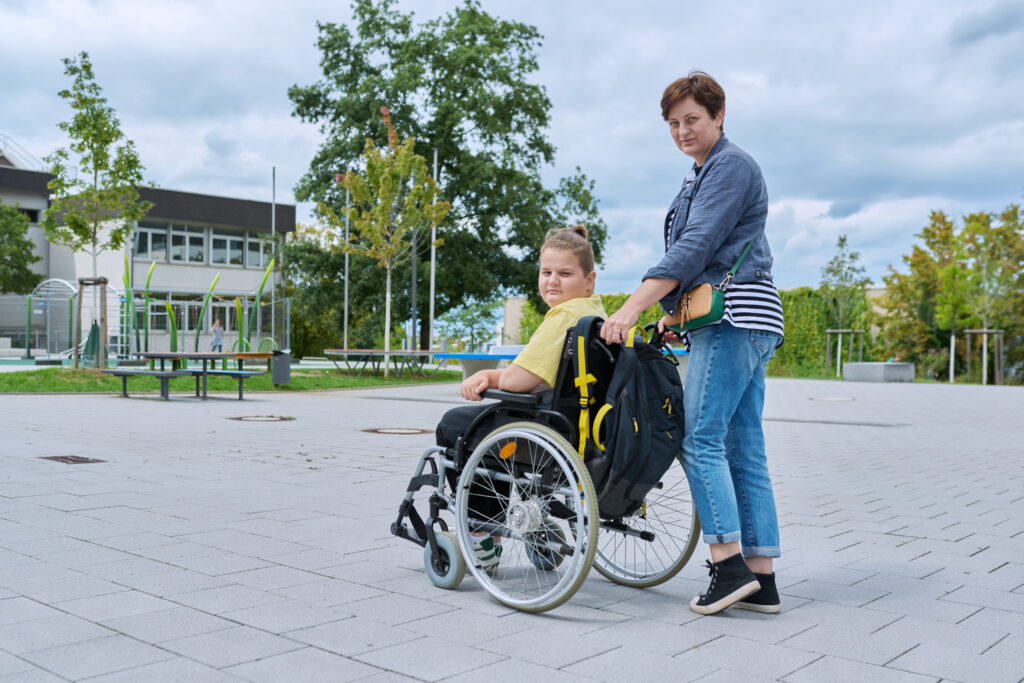 back view of woman with boy in wheelchair near school building back view of woman with boy in wheelchair near school building