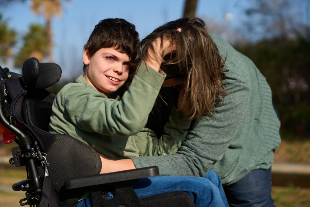 boy with cerebral palsy playing with his mother's hair in a wheelchair in the park boy with cerebral palsy playing with his mother's hair in a wheelchair in the park