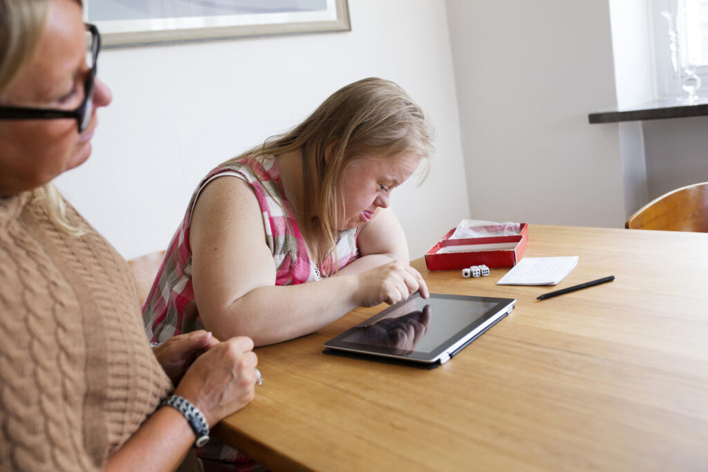 daughter with down syndrome using digital tablet, mother looking daughter with down syndrome using digital tablet, mother looking