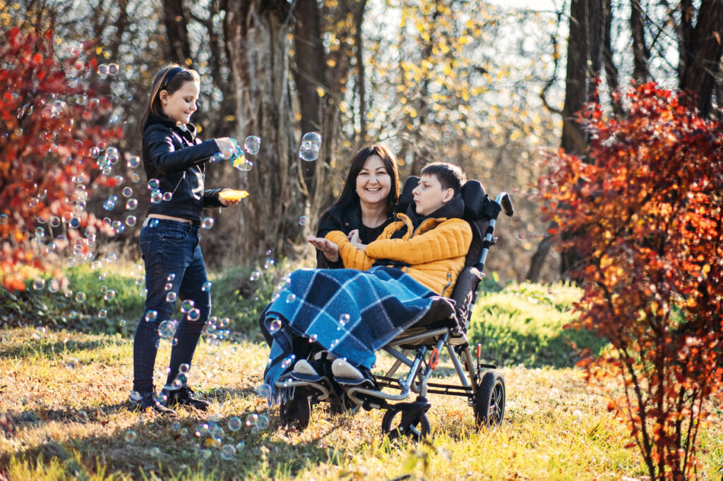 mother and sibling playing with bubbles with child in wheelchair, inclusive outdoor play, disability support, family bonding, adapted activities. mother and sibling playing with bubbles with child in wheelchair, inclusive outdoor play, disability support, family bonding, adapted activities.